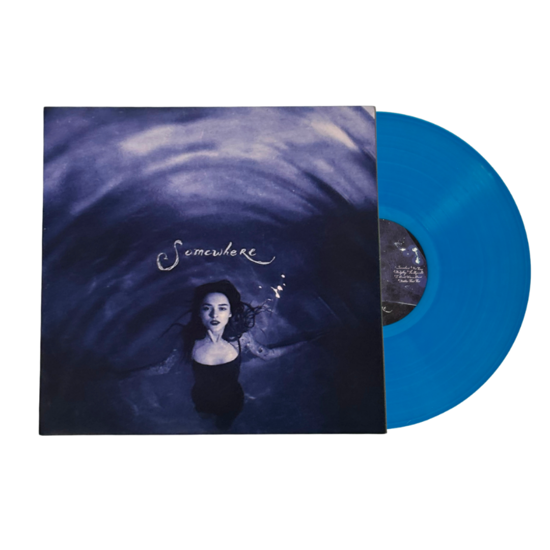 A vinyl record partially pulled from its sleeve, showing a bright translucent blue disc alongside the album cover art featuring a woman in water with the title 'Somewhere' in script.