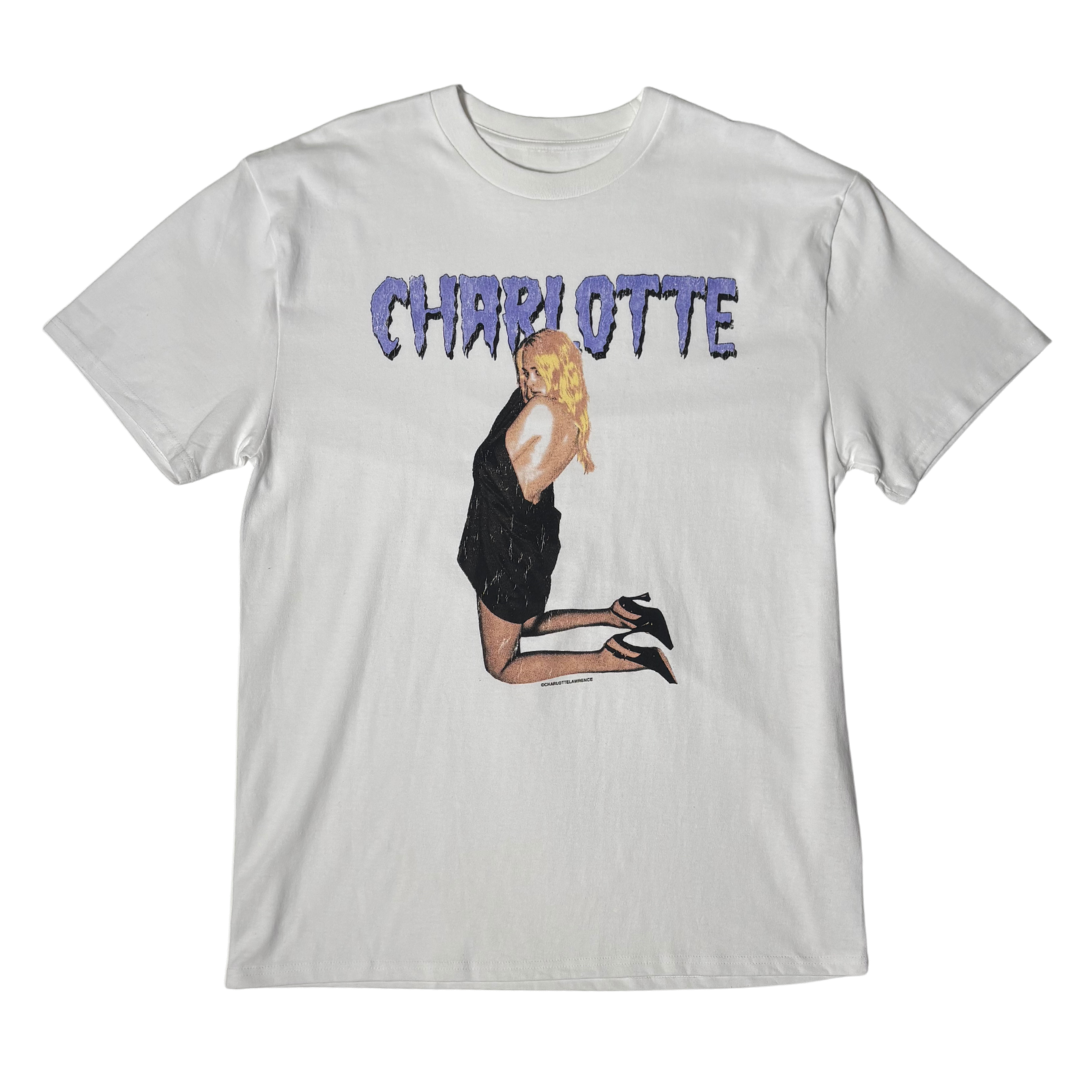 A light gray short-sleeve t-shirt featuring a graphic print of a blonde woman in a black dress kneeling, with the word 'CHARLOTTE' printed above in a textured purple font.